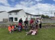 A group of people, including adults and children, gather outside on a lawn in a residential area.