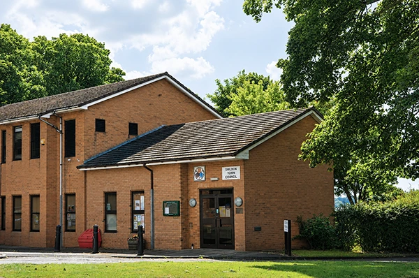 A brick town council building with trees and grass under a partly cloudy sky.